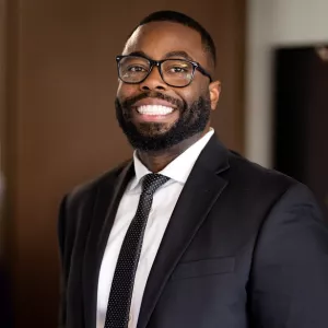 Titus Karvon smiling wearing a suit and glasses